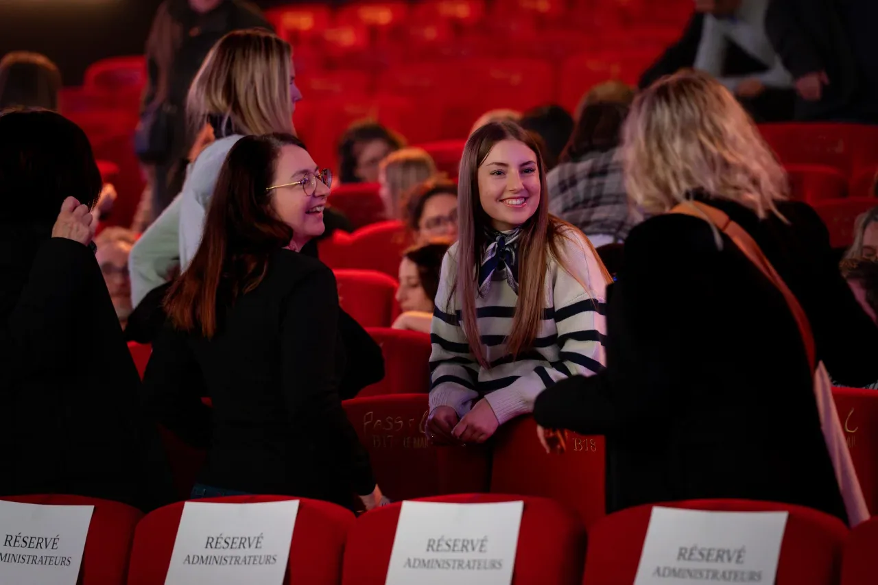 Participantes souriantes dans les fauteuils rouges d'un théâtre, convention Pluralis