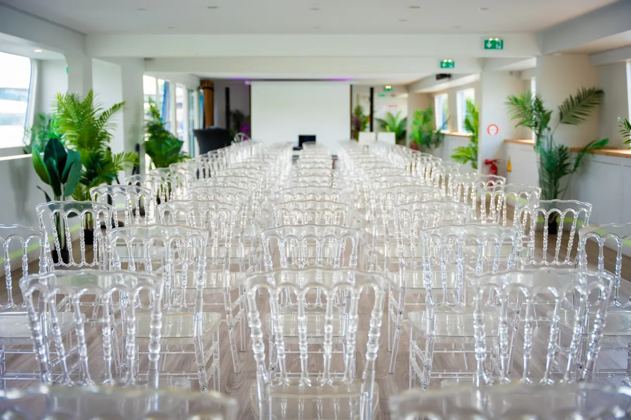 Salle de conférence prête : rangées de chaises transparentes bordées de plantes vertes