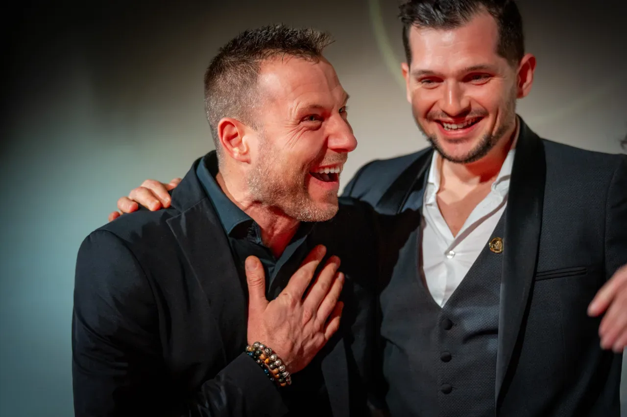 Deux invités hilares, bras sur l'épaule, lors d'une soirée de gala