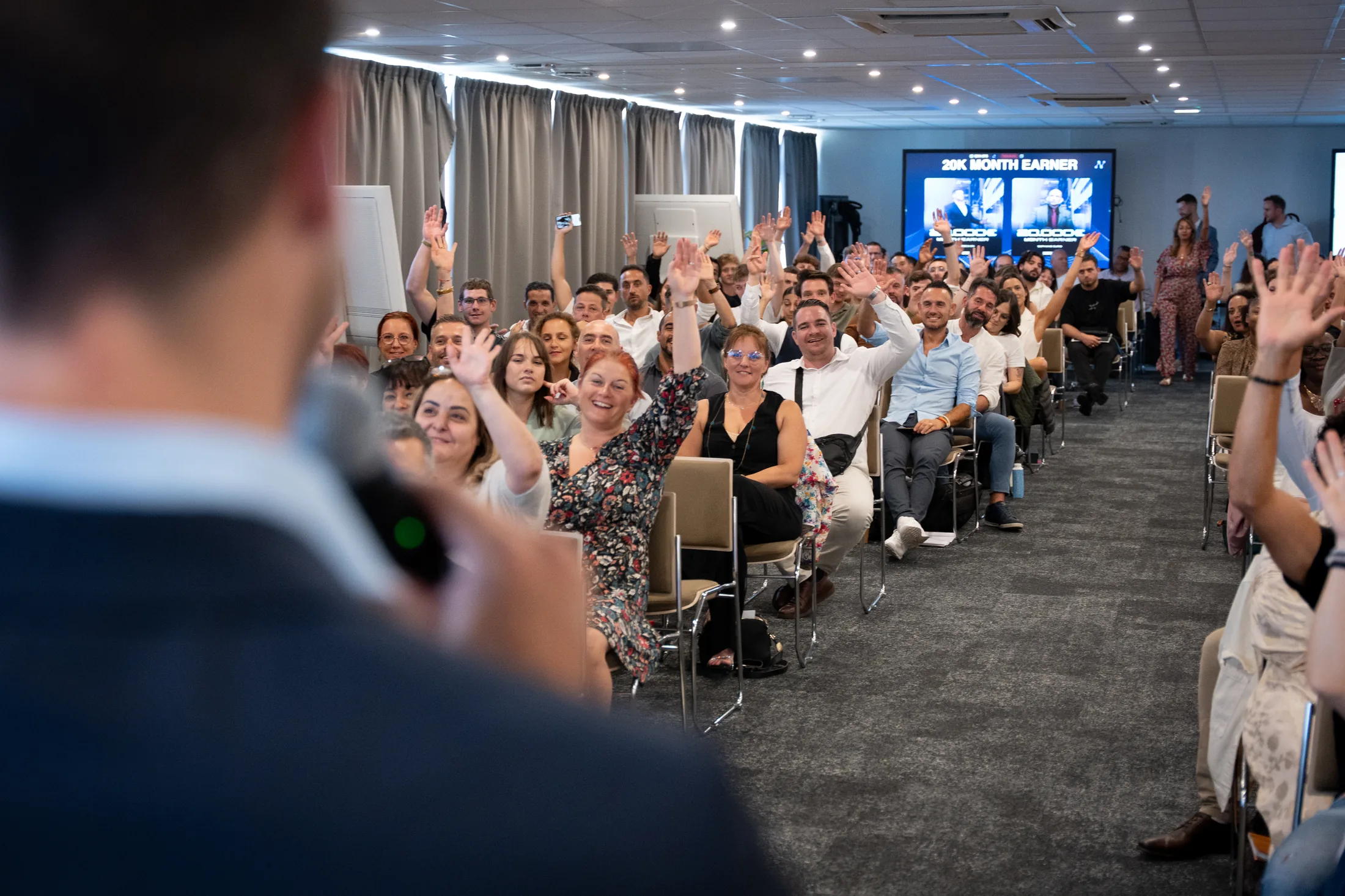 Salle de convention pleine, participants levant la main