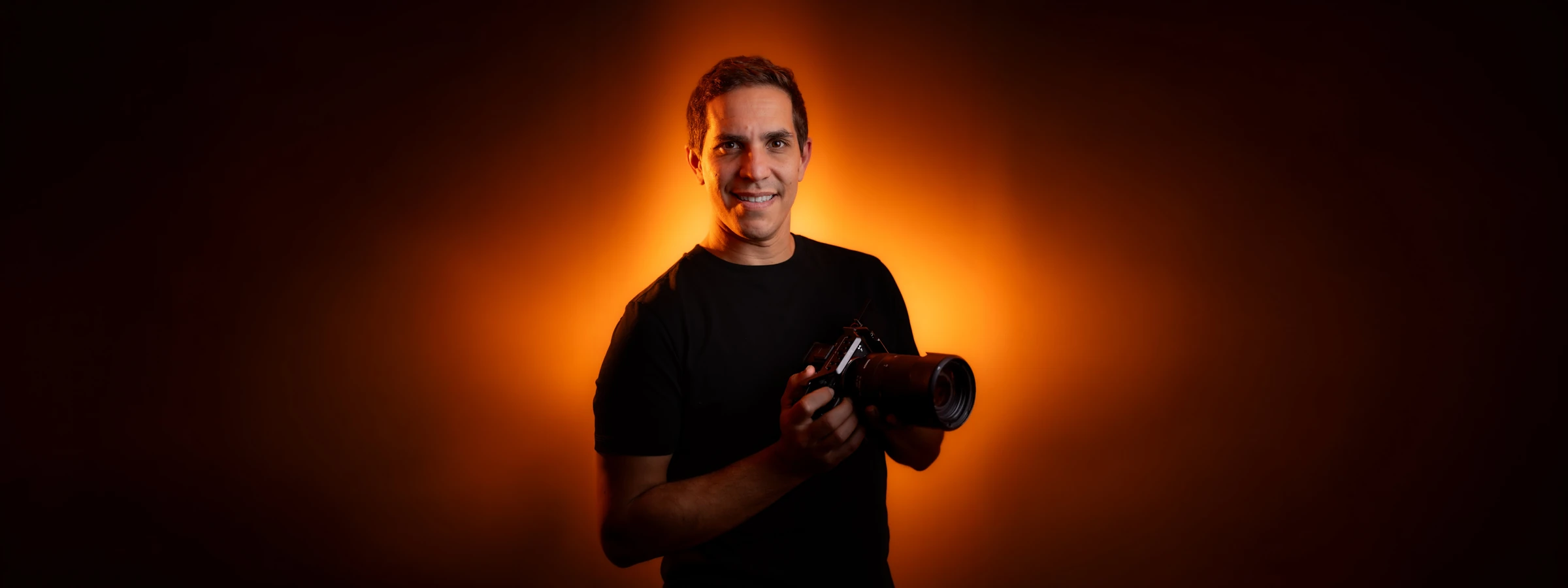 Robin Sforza, photographe et vidéaste à Grenoble, sourire et appareil photo en main sur un halo orange